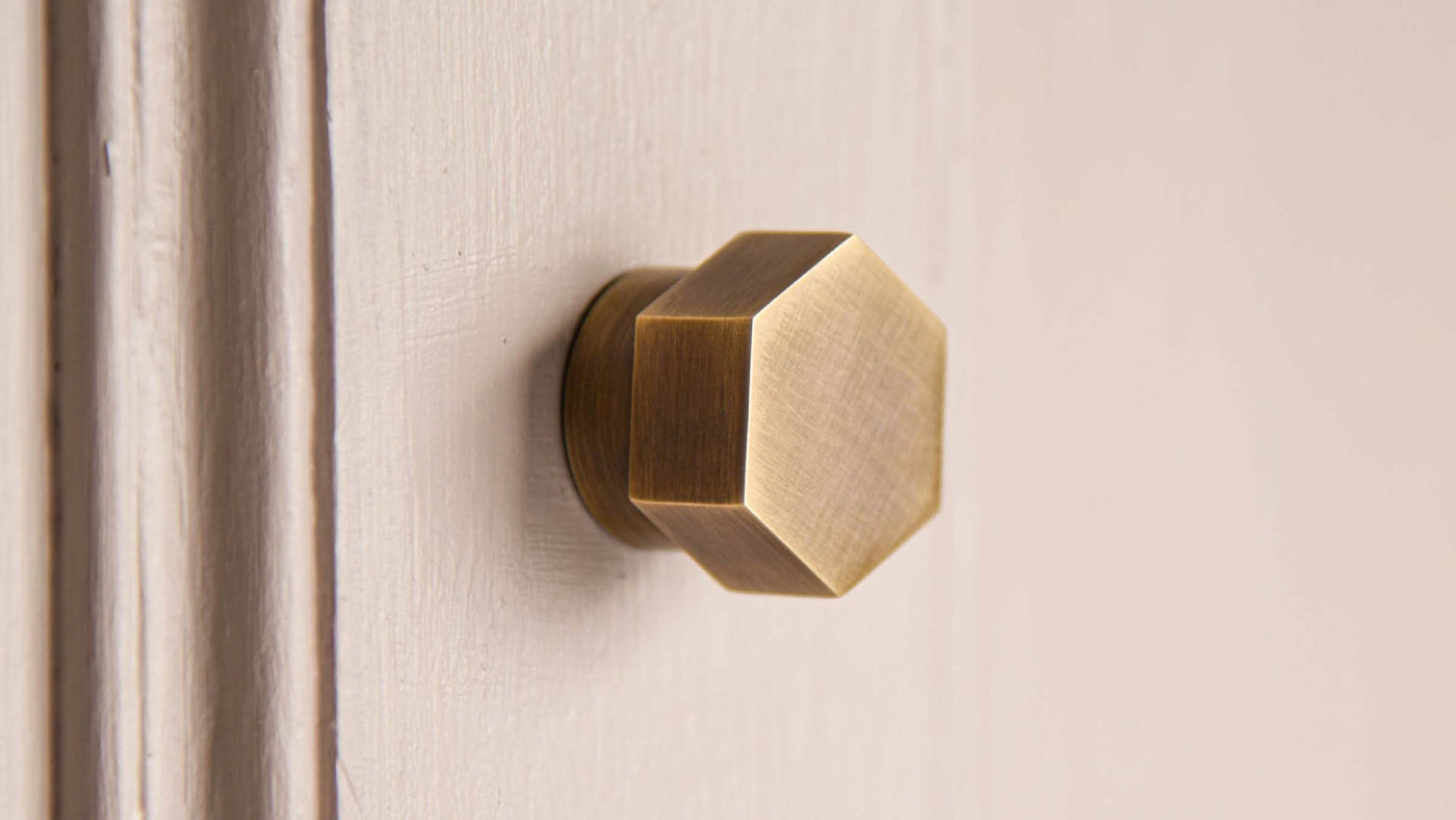 Light Antique Brass finishes seen on a Hex cupboard knob on a pink cupboard
