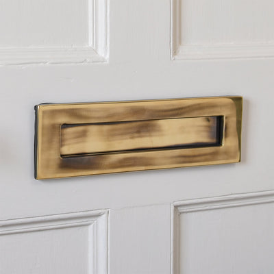 Brass letterplate with darker aged finish on a painted door