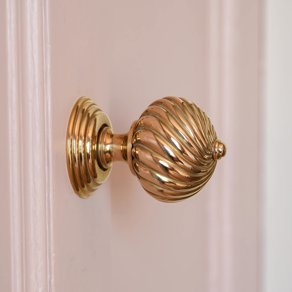 Polished brass swirl detail door handles on pink door