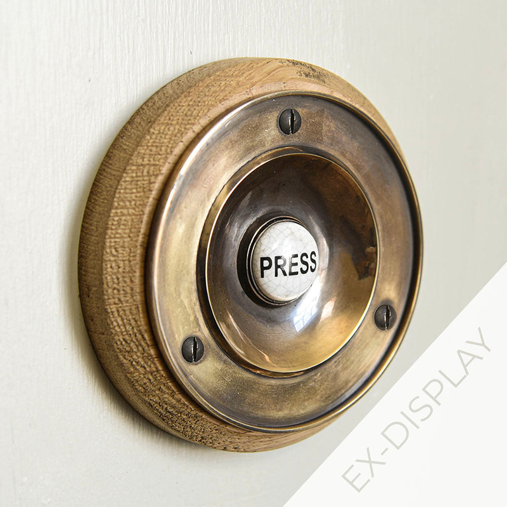 Polished antique brass bell press on an oak backplate  on a light grey surface with a watermark and ex display text in the corner