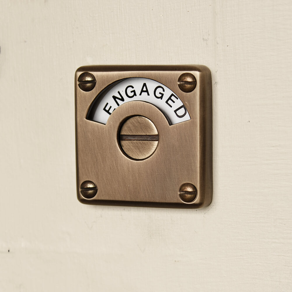 brass bathroom slide bolt showing the front face with the word engaged viewable on the dial