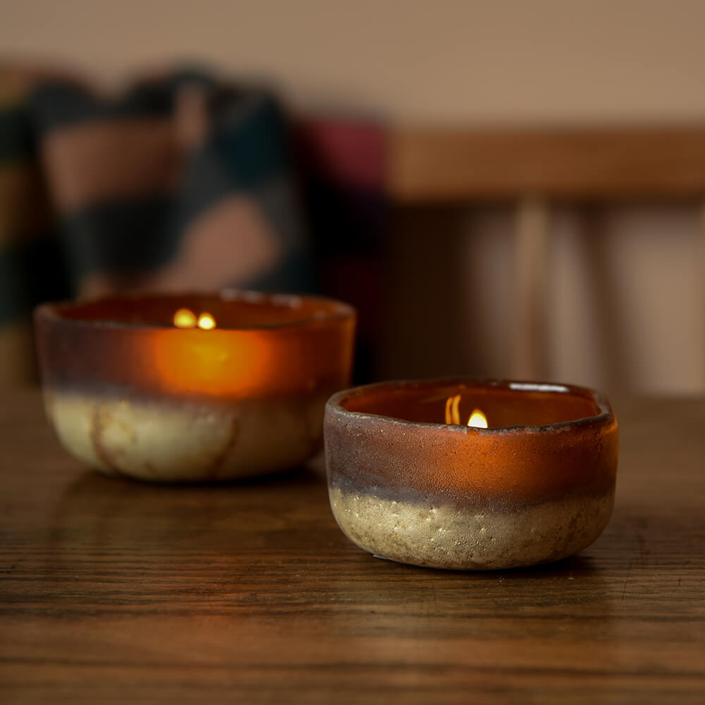 Pair of glass tea light holders with candles, on a rustic kitchen table