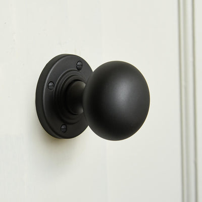 Smooth black round door knob with reeding to the neck of the roseplate mounted on a cream door