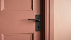Black door handle on a two tone pink door/wall