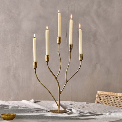 Antique brass 5 arm candelabra with 5 white lit candles on a table with a grey tablecloth against a grey wall