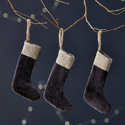 Charcoal set of 3 mini stocking decorations made from velvet with a jute linen band at the top. Hanging from jute rope on a copper wire against a dark blue background