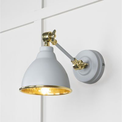 Hammered brass Brindley wall light in off-white against a white panelled wall