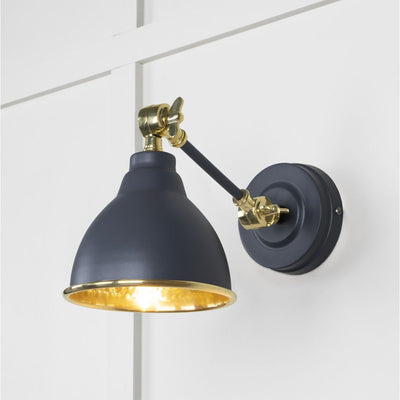 Hammered brass Brindley wall light in navy blue against a white panelled wall