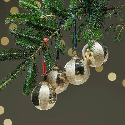 Set of 4 gold glass baubles with etched detailing hanging from a christmas tree branch with different coloured ribbon against a dark green background