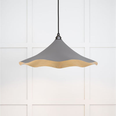 Smooth brass flora pendant light in bluff hanging from a black fabric cable against a white panelled wall