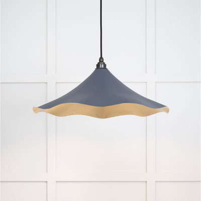 Smooth brass flora pendant light in slate hanging from a black fabric cable against a white panelled wall