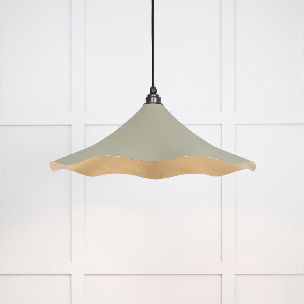 Smooth brass flora pendant light in tump hanging from a black fabric cable against a white panelled wall