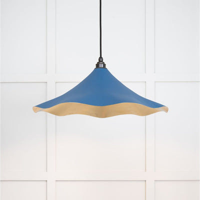 Smooth brass flora pendant light in upstream hanging from a black fabric cable against a white panelled wall