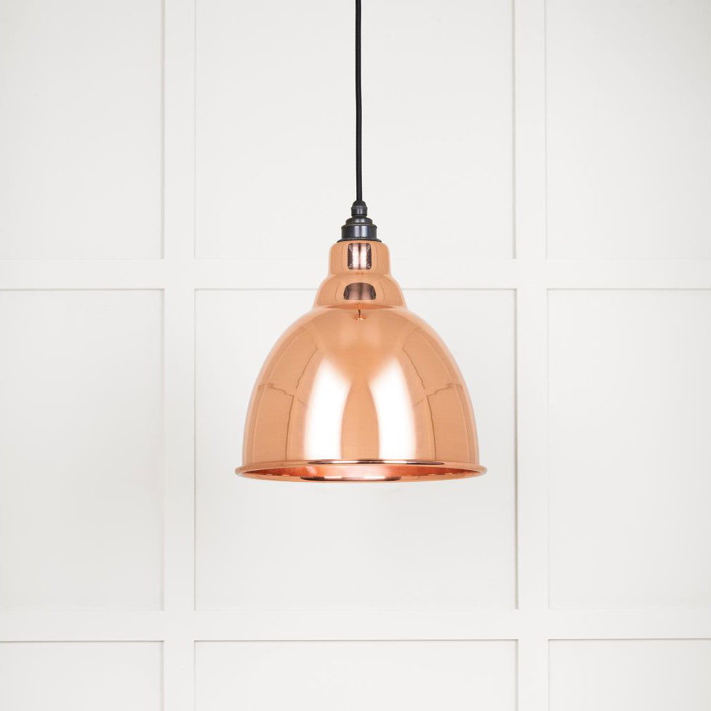 Smooth solid copper Brindley pendant light hanging from a black fabric cord against a white panelled wall