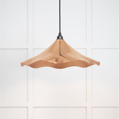 Smooth copper pendant light hanging from a black fabric cord against a white panelled wall