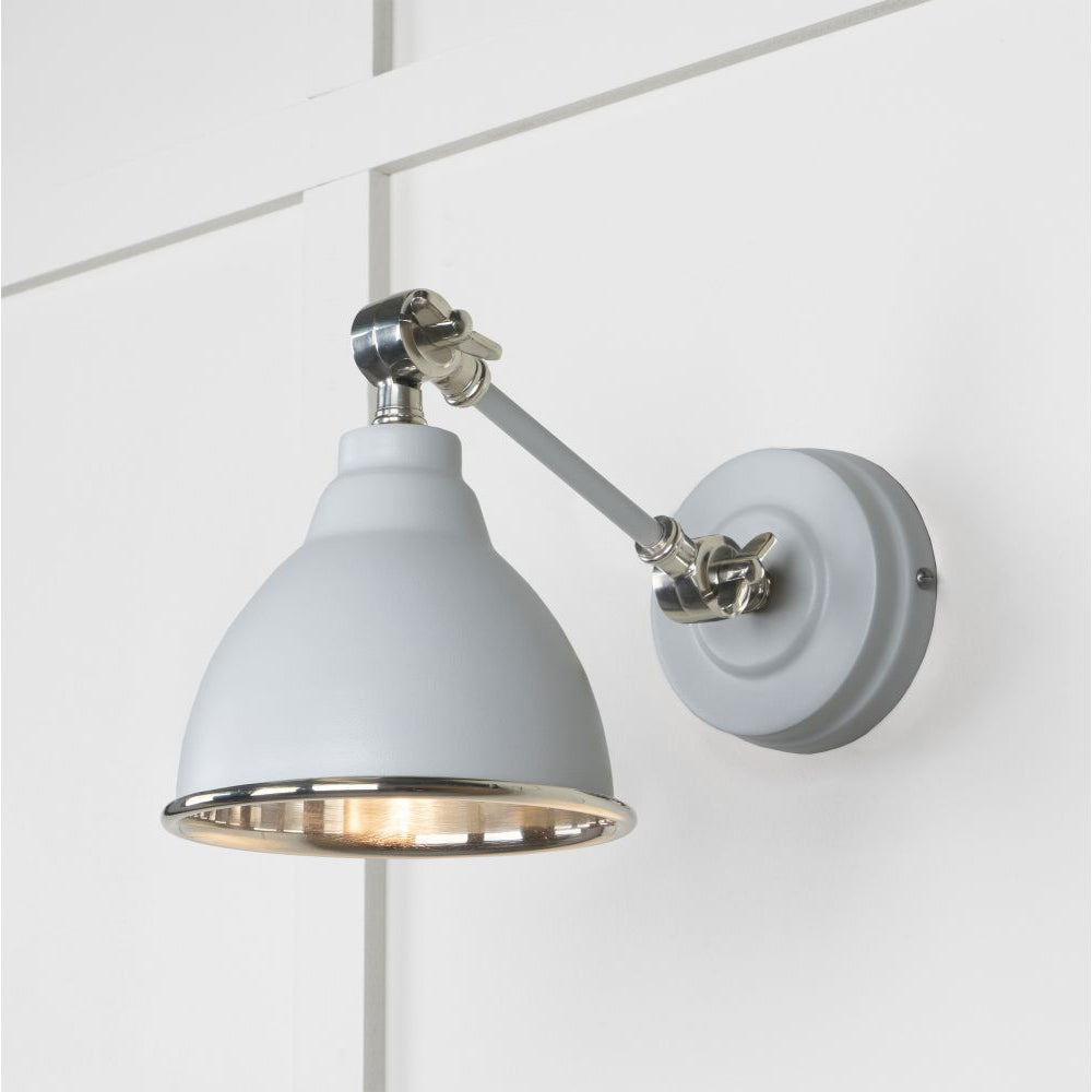 Smooth nickel Brindley wall light against a white panelled wall with the light switched on