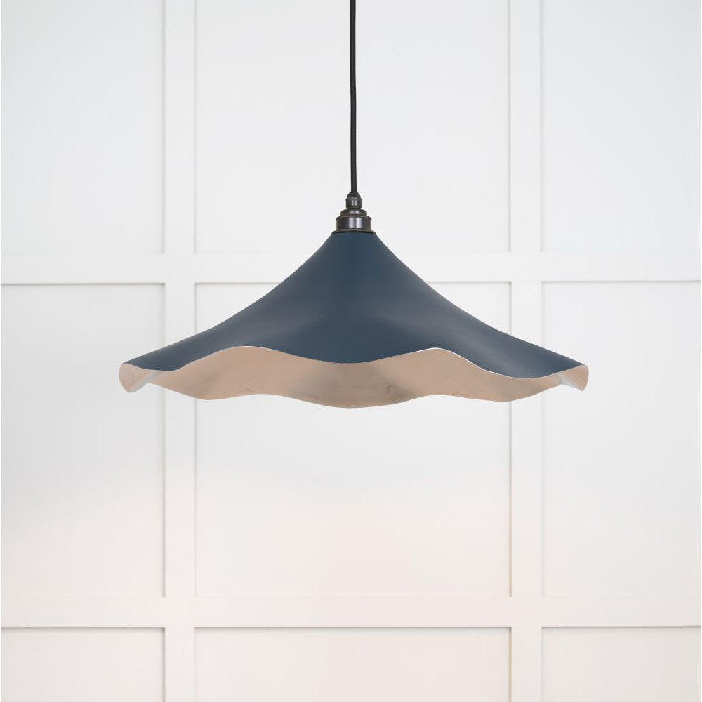 Smooth nickel flora pendant light in dusk hanging from a black fabric cord against a white panelled wal