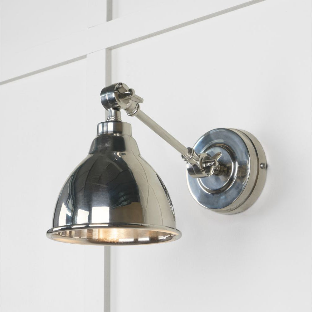 Polished nickel wall light, lit up against a white panelled wall