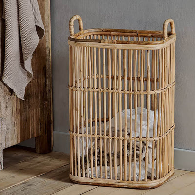 Rattan laundry basket with handles next to a wooden unit with a grey towel hanging down and sat on a wooden floor