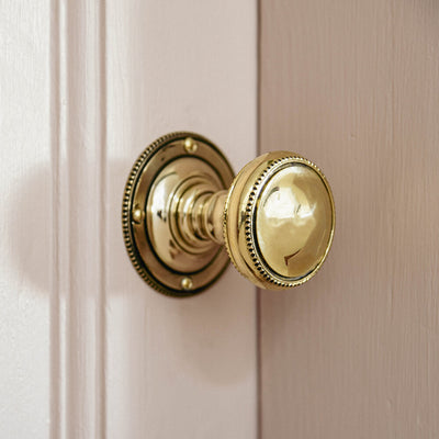 Beaded edge door knob in brass on a pink door