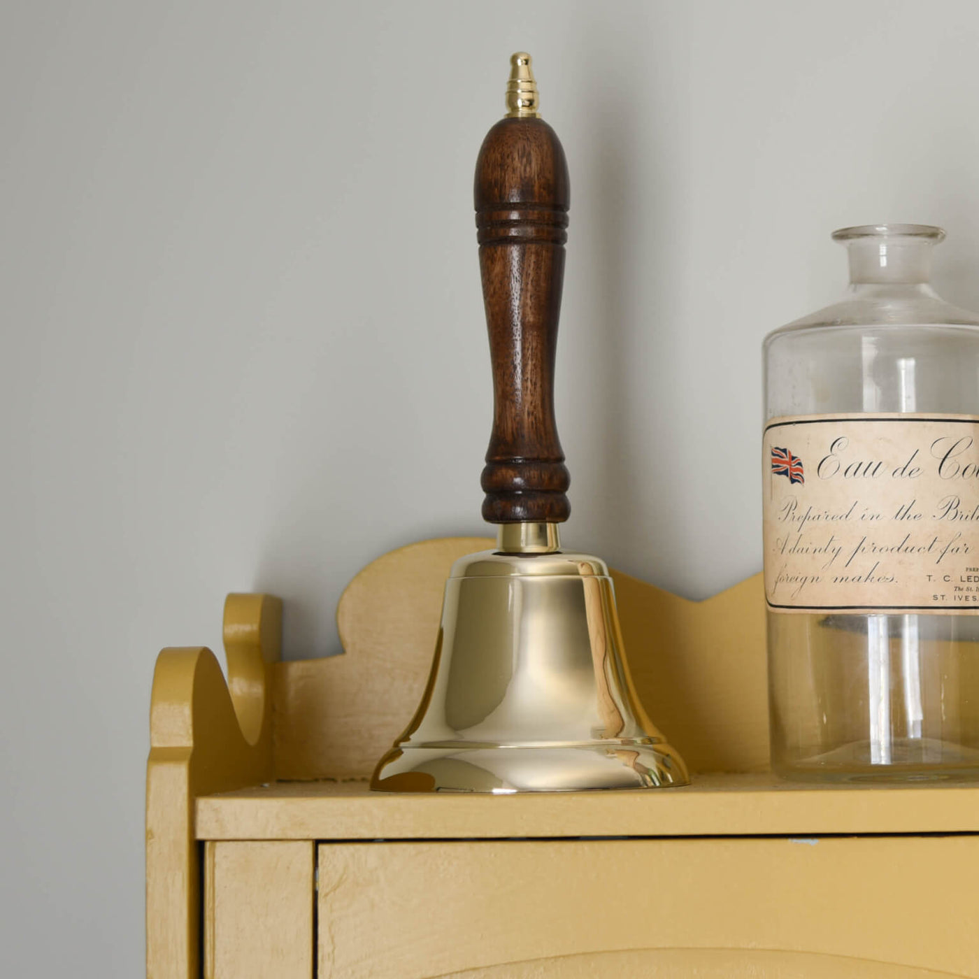 Brass Hand Bell with wooden handle on yellow cabinet, perfect for hotel and receptions 