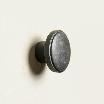 A flat round cabinet knob in a black beeswax finish
