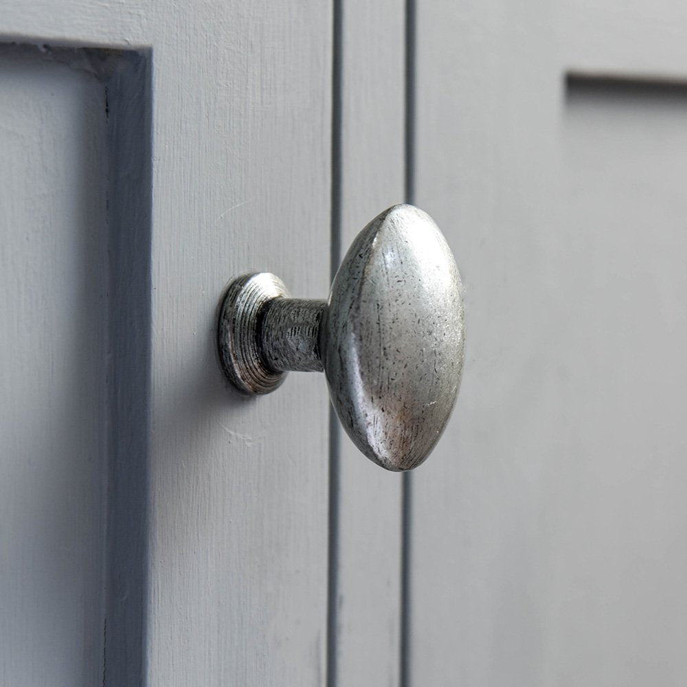An oval cabinet knob in a pewter patina finish fitted to a cupboard door