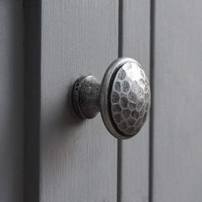 A cabinet knob in a pewter beaten finish fitted to a cupboard door