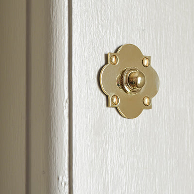Solid brass Quatrefoil Bell Push on cream door from afar.