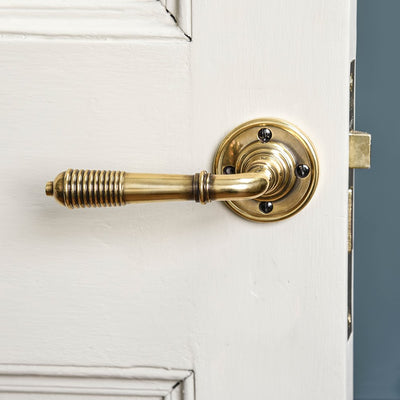 A reeded lever handle on a rose set backplate in aged brass fitted on a door