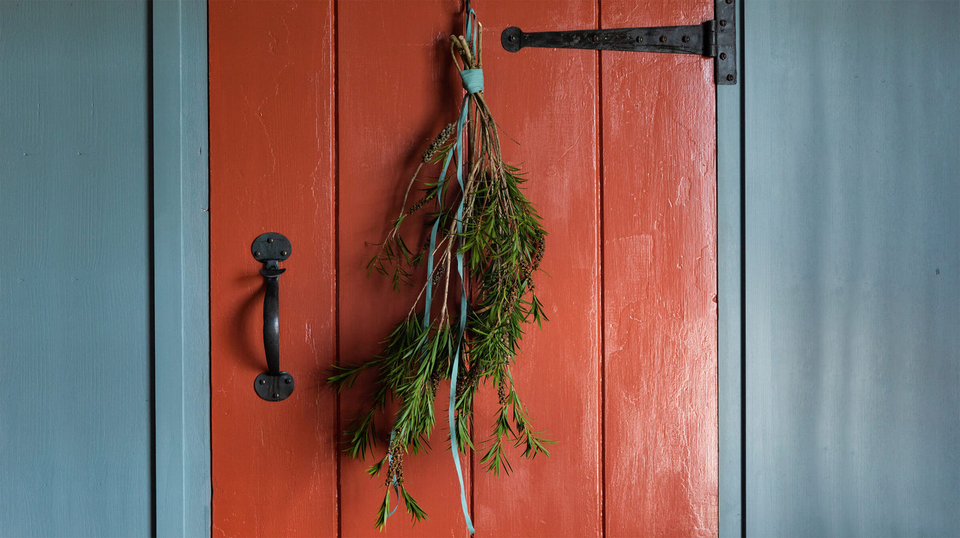 Red cottage door featuring iron traditional fittings and a natural wreath