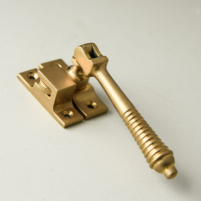 Casement fastener in aged brass with reeded detail to the drop handle and a hook plate fastener