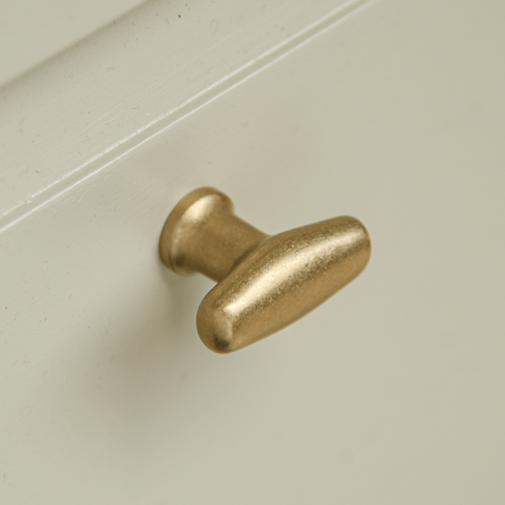 Soft edge oblong cabinet handle in an aged brass finish on cream drawer