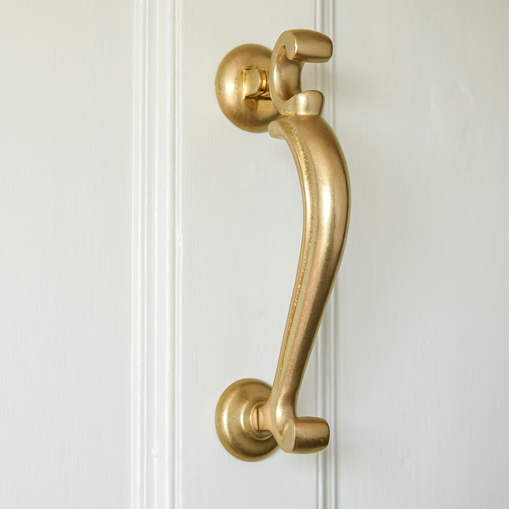 Brass door knocker on cream front door in aged brass with a slender decorative form and smooth central piece