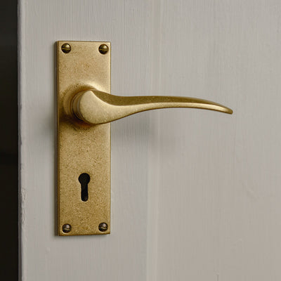 Aged brass penwerris curved lever handle on a cream door