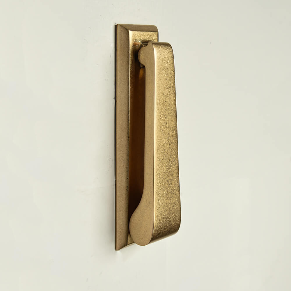 Slim door knocker in rectangular form with a mottled aged brass uniform finish