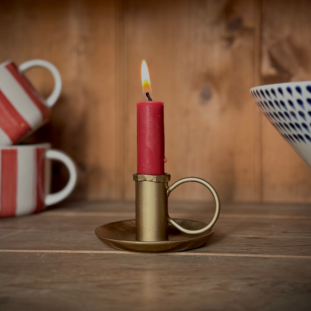 Brass coloured candle stick with burning red candle in it