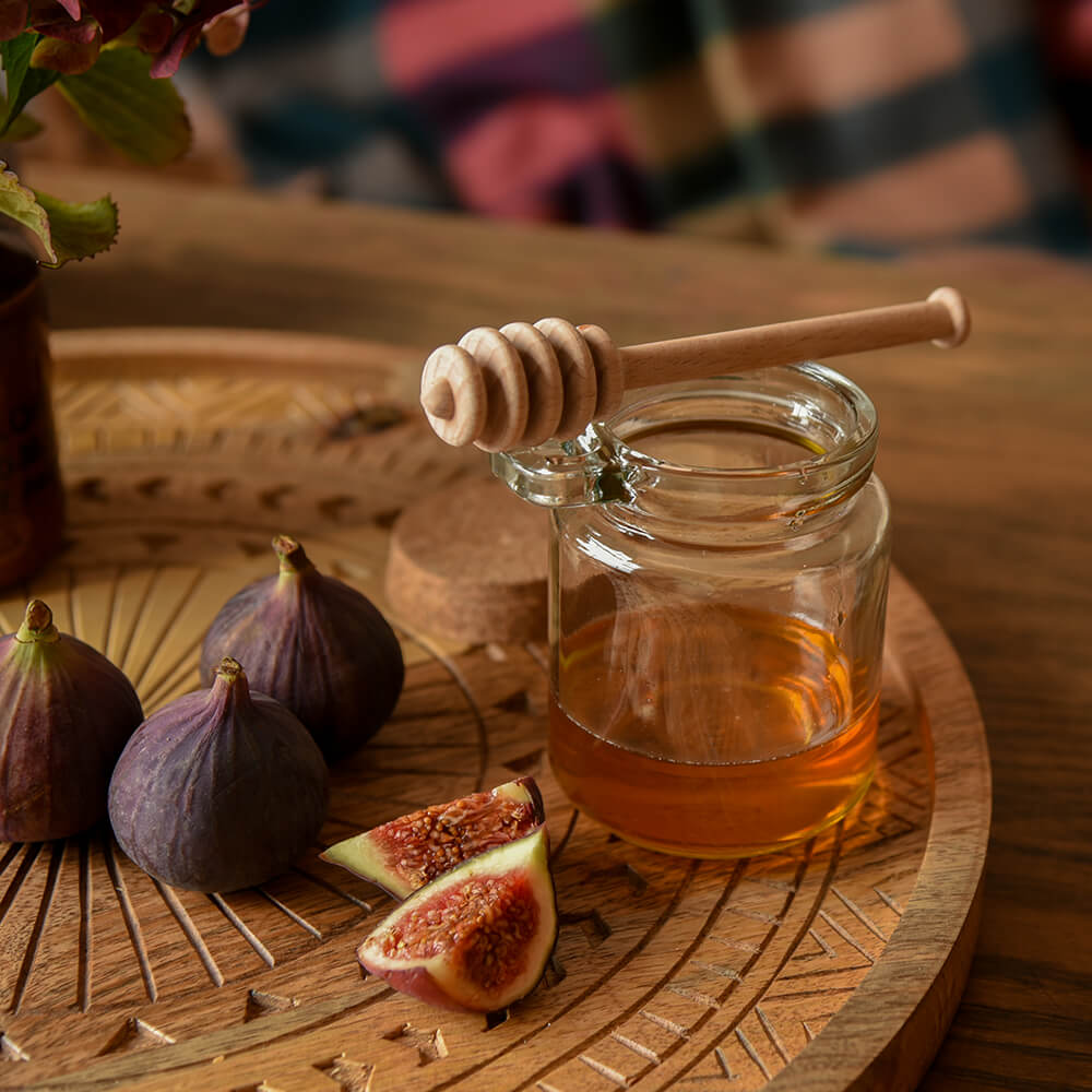 Honey drizzler on a clear jar with figs on a carved wooden tray