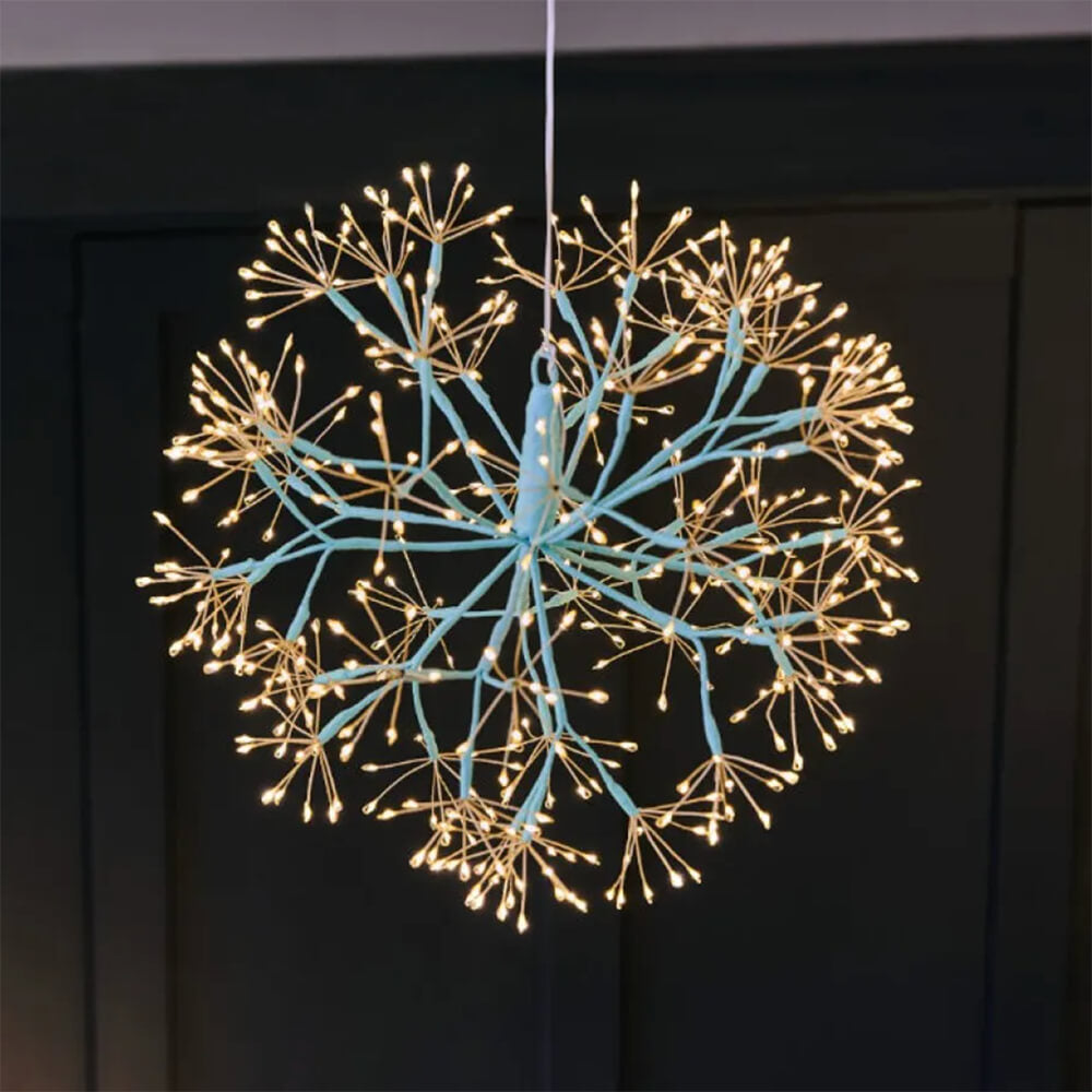 Decorative light fixture shaped like a snowflake with blue center and gold branches on a dark background