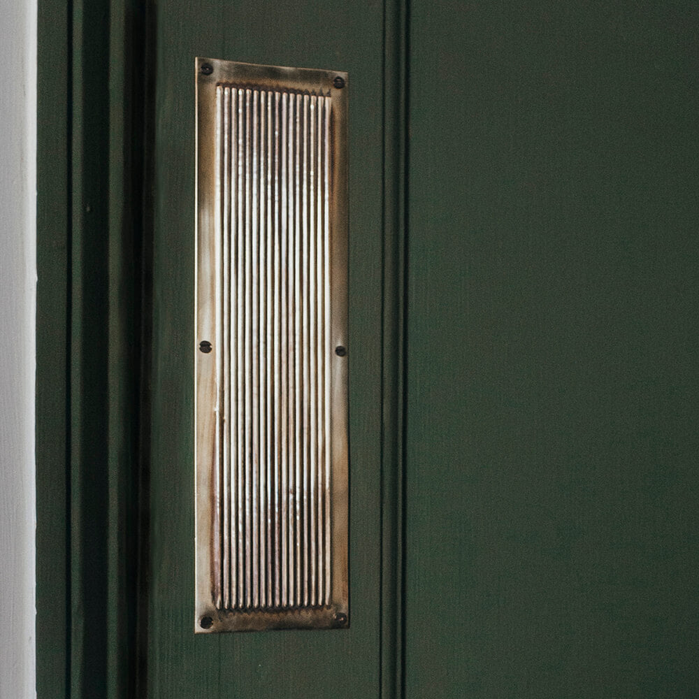 Aged brass rectangular fingerplate with reeded detailing mounted onto a dark green door