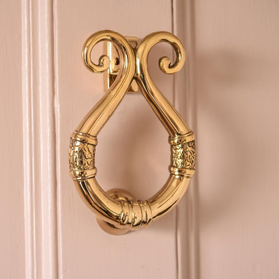Solid brass looped door knocker in situ against a pale pink panelled door