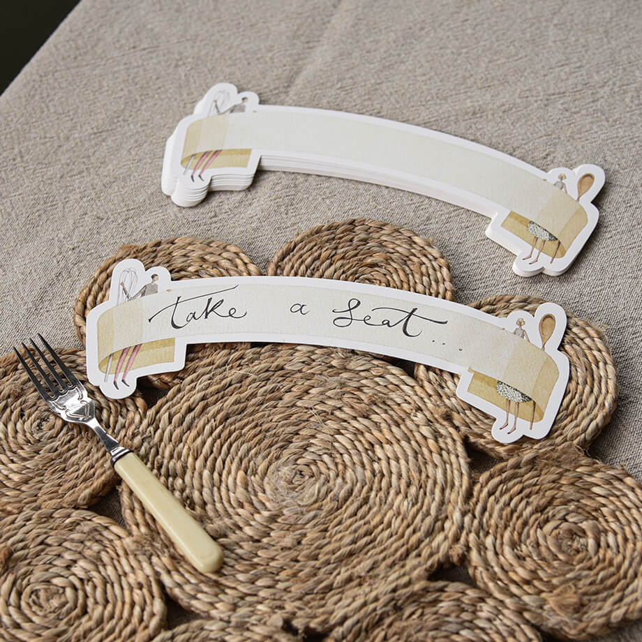 Decorative place card holder with 'Take a Seat' text on a textured surface with a fork.