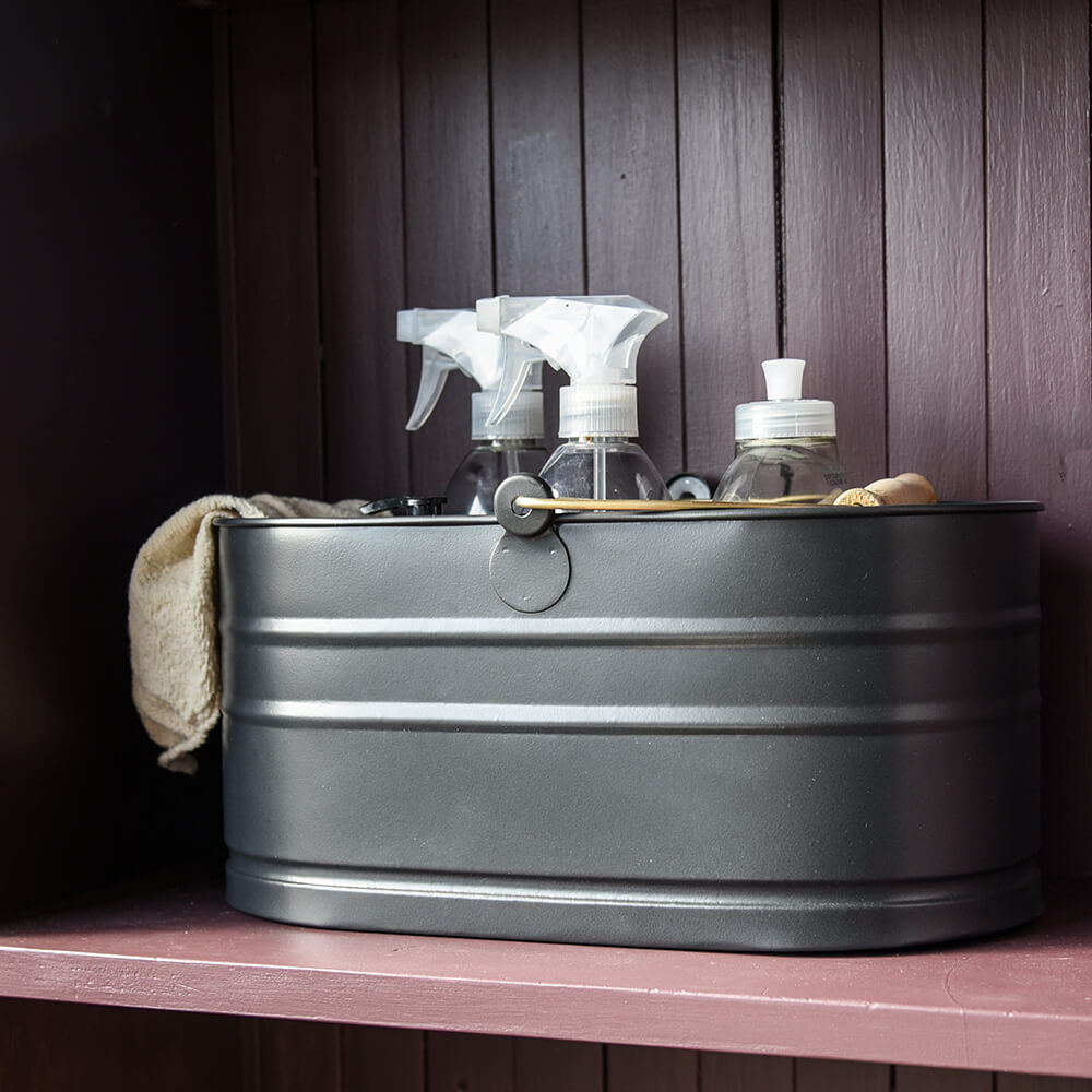 Metal trough with cleaning supplies on a wooden surface against a dark wooden panel background