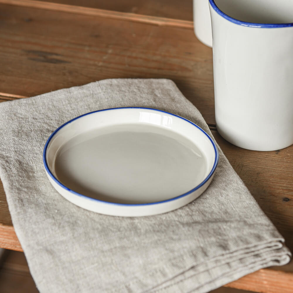 White ceramic dish with blue rim on a wooden surface with a white mug.