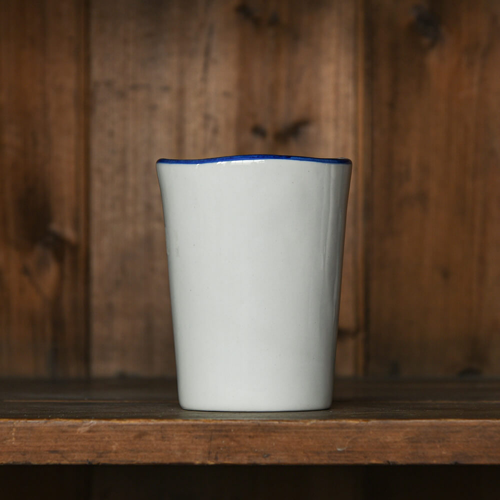 White ceramic cup with blue rim on a wooden shelf