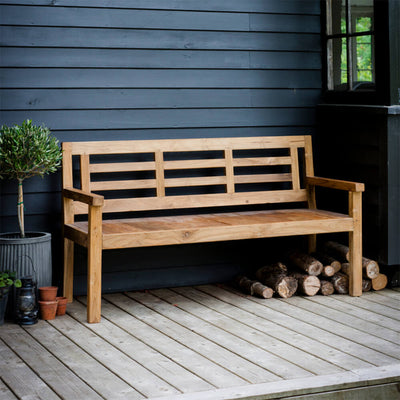 Teak-bench-infront-of-wooden-house-with-logs-beneath