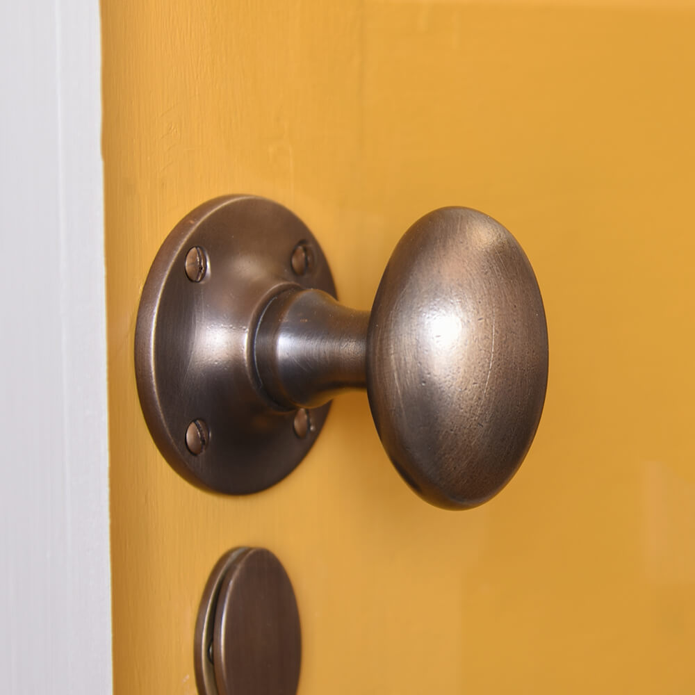 oval shaped door knobs in distressed antique brass seen on a mustard yellow door with matching escutcheon