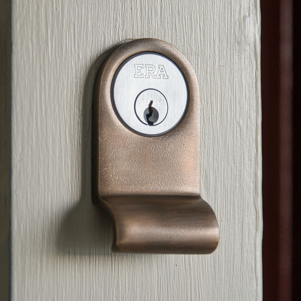 Distressed antique brass cylinder latch pull with a yale lock on a cream painted background