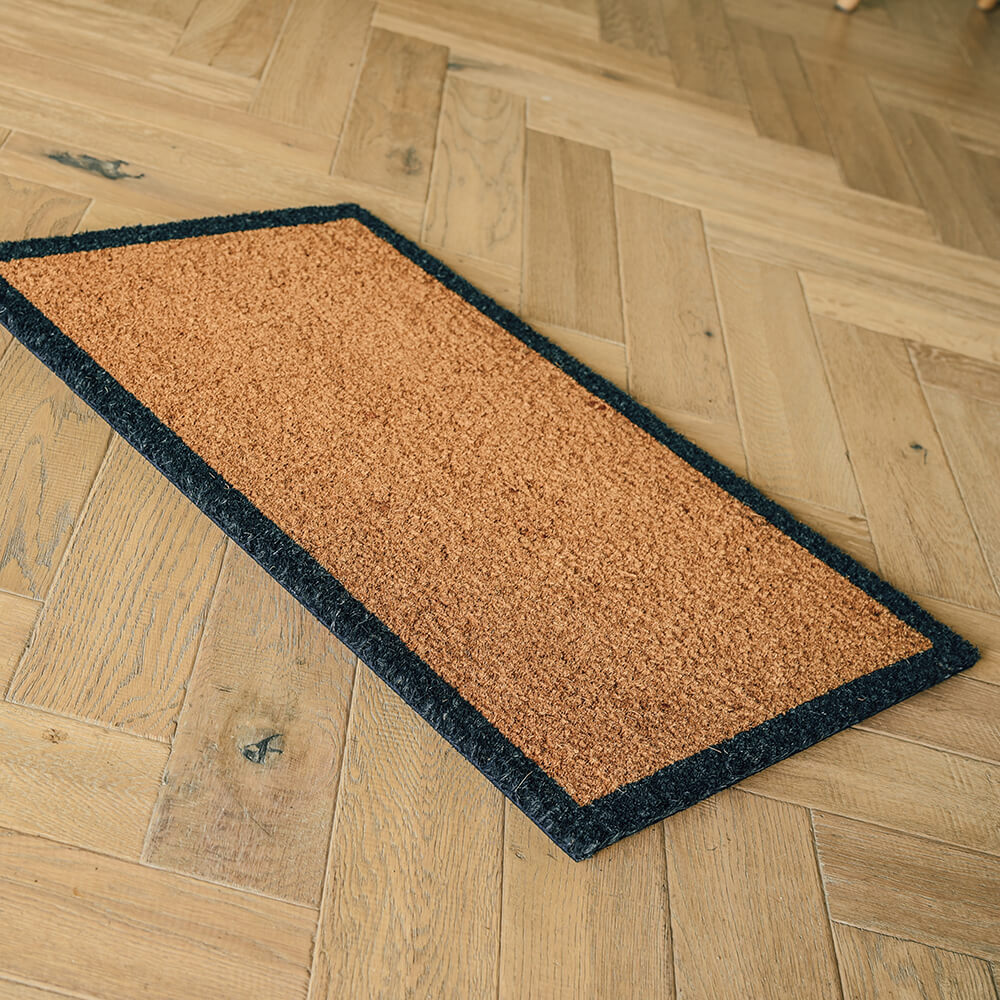 Brown doormat with black border on a wooden floor