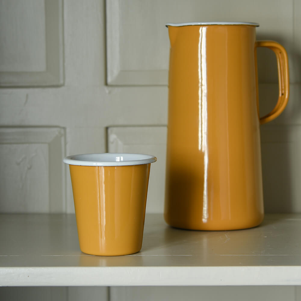 Mustard yellow enamel cup and tall jug on a cream shelf in a cabinet